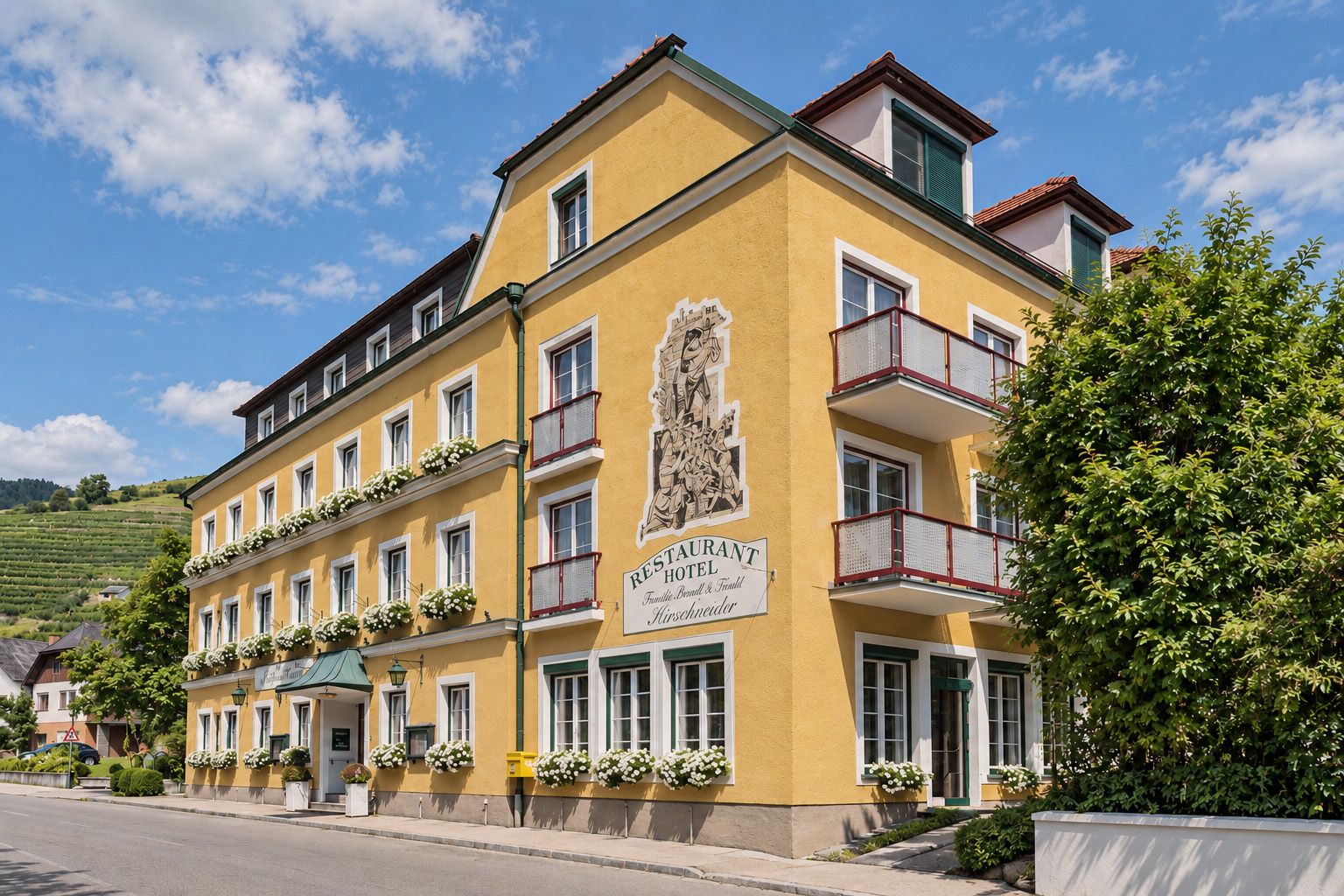 Exterior view of the Wachau Wine Hotel with its yellow facade, balconies, flowers, and restaurant sign in the Wachau region.