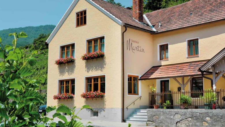 Exterior view of a yellow guest house with red roof tiles and flower boxes on the windows.