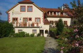 Ein gro&szlig;es, traditionelles Haus mit rotem Dach und bl&uuml;hendem Garten im Vordergrund.