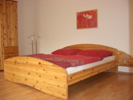 Schlafzimmer mit Holzbett und roter Bettwäsche.